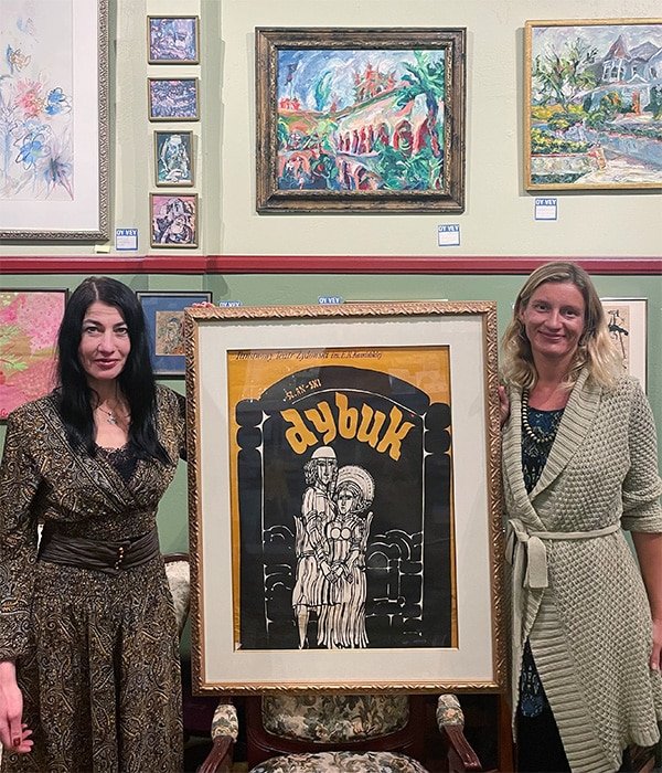 Two women holding up a framed artwork