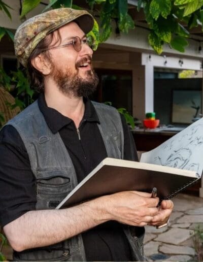 Oleg Tsank smiling while sketching during a Yiddish portrait session outdoors at Yiddishland California.